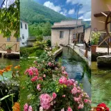 A picturesque village with a clear stream flowing through it, lined with flowers and old buildings.