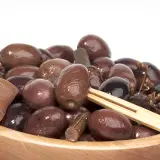 Olive nere sotto sale, un assaggio della ricetta marchigiana. Un piatto di olive scure e lucide in una ciotola di legno.