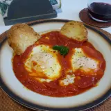 Uova in trippa marchigiana, un piatto saporito con uova in camicia su un letto di sugo rosso, guarnito con pane tostato e prezzemolo.