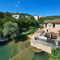 Sassoferrato cosa vedere: un antico mulino ad acqua lungo un fiume, con case e vegetazione lussureggiante sullo sfondo.