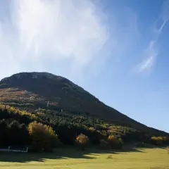 Ampio prato verde ai piedi del monte san vicino, con boschi autunnali e cielo azzurro.