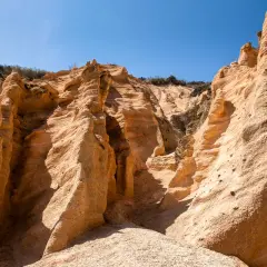 Formazioni rocciose color ocra, scolpite dal vento, sembrano **le lame rosse** di un canyon desertico sotto un cielo azzurro intenso.