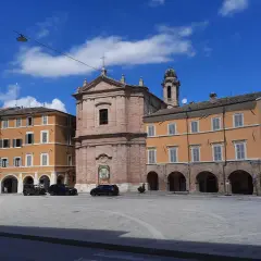 Piazza a San Severino Marche con edifici colorati, una chiesa in mattoni e cielo azzurro.