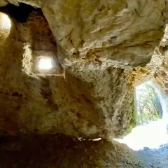 Interno della grotta del mortarolo, con aperture che illuminano le rocce calcaree e un'uscita verso il verde.