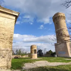 Torri antiche e un piccolo edificio circolare nel parco del cardeto, sotto un cielo azzurro con nuvole bianche.