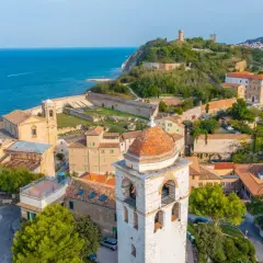 Vista aerea del **centro storico** di Ancona, con il mare blu, chiese, torri e case con tetti rossi.