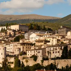Spello, un borgo umbro incastonato tra colline verdi, con case in pietra e torri antiche che si stagliano contro il cielo azzurro.