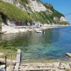 Scogli bianchi e mare cristallino alla spiaggia della Scalaccia. Una piccola barca è ormeggiata vicino a casotti colorati.