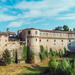 Un imponente palazzo storico con torri e mura di mattoni, circondato da vegetazione. Un luogo da scoprire: Urbania cosa vedere.
