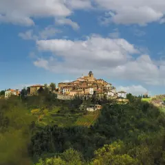 Borgo antico su un colle, con case in pietra e tetti rossi, sotto un cielo azzurro con nuvole bianche. Il **monte Grimano** domina il paesaggio.