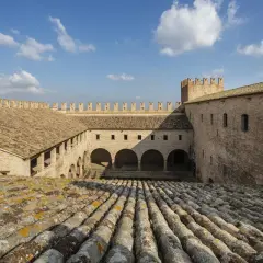 Cortile interno di un castello a Tolentino, Marche, con tetti in cotto e cielo azzurro.