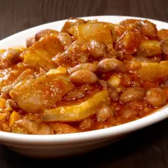 Piatto fumante di fagioli con le cotiche, un classico della ricetta marchigiana, servito in una ciotola bianca su un tavolo di legno scuro.