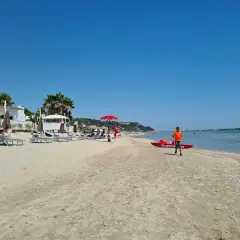 Sole splendente sulla campofilone spiaggia, con bagnanti rilassati, ombrelloni e un bagnino pronto a intervenire vicino a una barca di salvataggio.