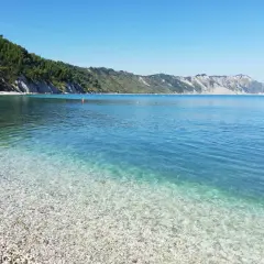 Acque cristalline e ciottoli bianchi a Portonovo, una delle spiagge più belle d'Italia. La costa verdeggiante si tuffa nel mare azzurro.