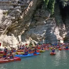 Gente in kayak esplora un canyon con pareti rocciose imponenti, simili a marmitte dei giganti nelle Marche.