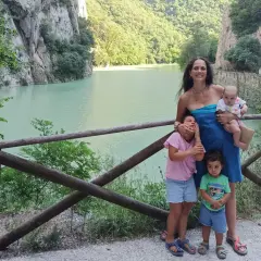 Famiglia felice nella golena del Furlo, con un lago turchese e montagne verdi sullo sfondo.