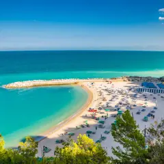 Spiagge Sirolo con acque turchesi, sabbia dorata, ombrelloni e gente che si gode il sole.