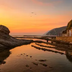 Tramonto dorato sulla spiaggia del Passetto, con rocce scolpite e archi colorati che si riflettono nell'acqua calma.