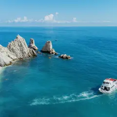 La spiaggia delle Due Sorelle, con le sue iconiche rocce, accoglie bagnanti e kayak. Una barca solca il mare azzurro.