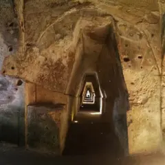Interno della grotta della Sibilla: un corridoio stretto e trapezoidale scavato nella roccia, con nicchie e aperture.
