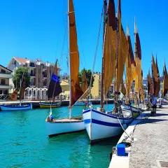 Barche a vela ormeggiate in un porto con case colorate sullo sfondo. Un dilemma: meglio Bellaria o Igea Marina?