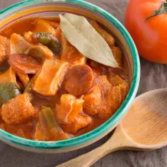 Un invitante piatto di trippa alla marchigiana, con peperoni e pomodoro, pronto per essere gustato con un cucchiaio di legno.