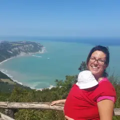 Donna sorridente con bimbo in fascia, ammira la costa del Conero dai sentieri. Perfetto per esplorare i sentieri del Conero con bambini.