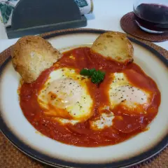 Uova in trippa marchigiana, un piatto saporito con uova in camicia su un letto di sugo rosso, guarnito con pane tostato e prezzemolo.