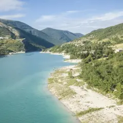 Spiaggia libera sul lago di Fiastra, con acque turchesi e montagne verdi sullo sfondo. Un luogo ideale per rilassarsi e godersi la natura.