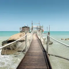 Ponte in legno verso un trabucco, tipica struttura da pesca delle Marche, su un mare azzurro e limpido.