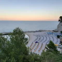 Spiaggia ordinata con lettini e ombrelloni, ideale per scoprire cosa vedere a Numana e Sirolo. Mare calmo al tramonto.