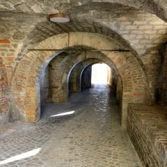 Arco in mattoni a Corinaldo, cosa vedere: un suggestivo passaggio coperto con pavimentazione in pietra e una porta rossa.