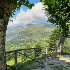 Panoramica mozzafiato del monte Monaco nelle Marche, con un sentiero serpeggiante e un cielo azzurro con nuvole bianche.