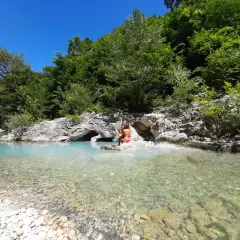 Bambini giocano nel **genga fiume** dalle acque cristalline, circondato da rocce e vegetazione lussureggiante.