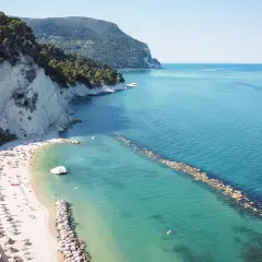 Spiaggia affollata con ombrelloni e lettini, scogliere bianche e mare azzurro a Porto Sant'Elpidio Mare.