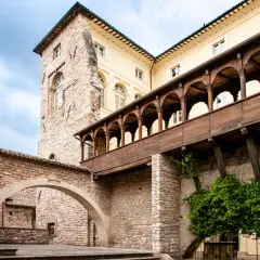 Cortile storico con archi in pietra e un loggiato in legno. Un assaggio di cosa vedere a Spello in un giorno, tra storia e natura.