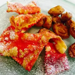 Cresciole marchigiane di Benedetta, dolci fritti cosparsi di zucchero a velo, con un tocco di rosso vivace.