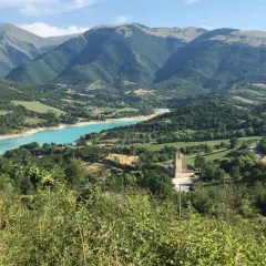 Panoramica del lago di Fiastra, con montagne verdi, un borgo e una chiesa. Cosa vedere in questo paesaggio mozzafiato.