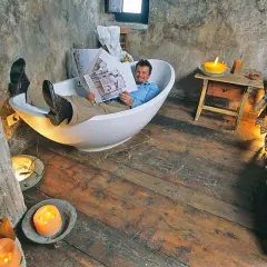 Uomo rilassato in vasca da bagno, legge un libro in un ambiente rustico, forse una casa vacanze a Santo Stefano, Abruzzo, con candele accese.