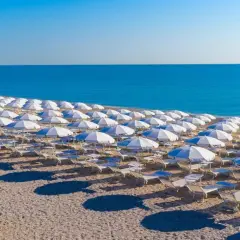 Filettate file di ombrelloni bianchi e lettini sulla spiaggia di Porto San Elpidio, con il mare azzurro sullo sfondo.