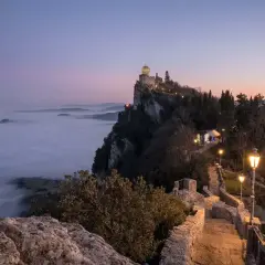 Torre Guaita domina la nebbia al tramonto, un invito a visitare San Marino per un'esperienza magica.