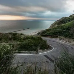 Strada panoramica che sale verso il tetto del mondo a Pesaro, con vista sul mare Adriatico e una costa verdeggiante.