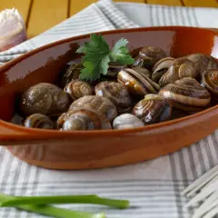Lumachine di mare in porchetta, un piatto gustoso servito in una ciotola di terracotta con aglio e prezzemolo.