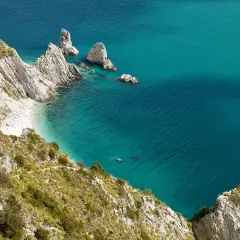Scogliere bianche e mare cristallino del Conero, con una piccola spiaggia nascosta e un nuotatore solitario.