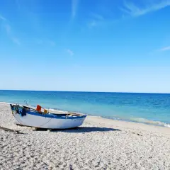 Barca bianca e blu sulla spiaggia di ciottoli a Senigallia, mare calmo e cielo azzurro.