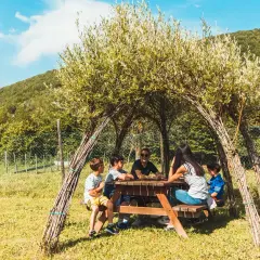 Bambini riuniti attorno a un tavolo da picnic sotto una tettoia naturale nel bosco dei folletti Urbania.