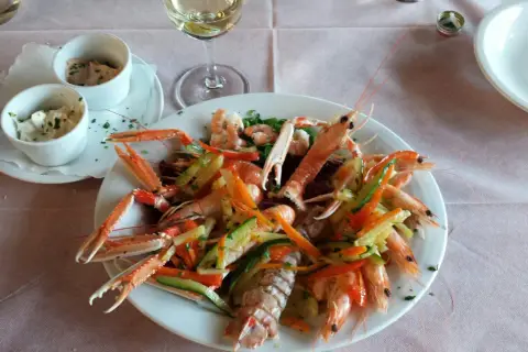 Un piatto di scampi e gamberi con verdure miste, un bicchiere di vino bianco e salse, un'ottima cena al conte Max Monte Roberto.
