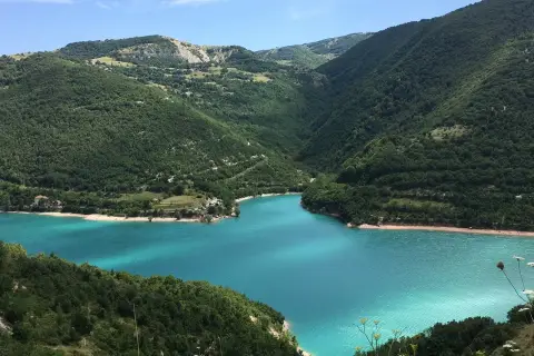 Splendido lago di Fiastra con acque turchesi, incastonato tra montagne verdi e rigogliose.