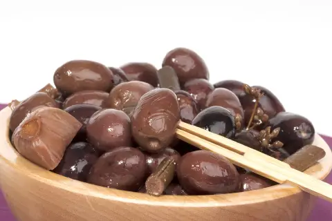 Olive nere sotto sale, un assaggio della ricetta marchigiana. Un piatto di olive scure e lucide in una ciotola di legno.