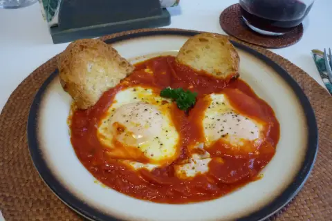 Uova in trippa marchigiana, un piatto saporito con uova in camicia su un letto di sugo rosso, guarnito con pane tostato e prezzemolo.